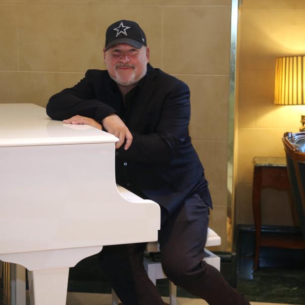 Ein Mann mit einer Dallas Cowboys-Kappe lehnt an einem weißen Klavier.