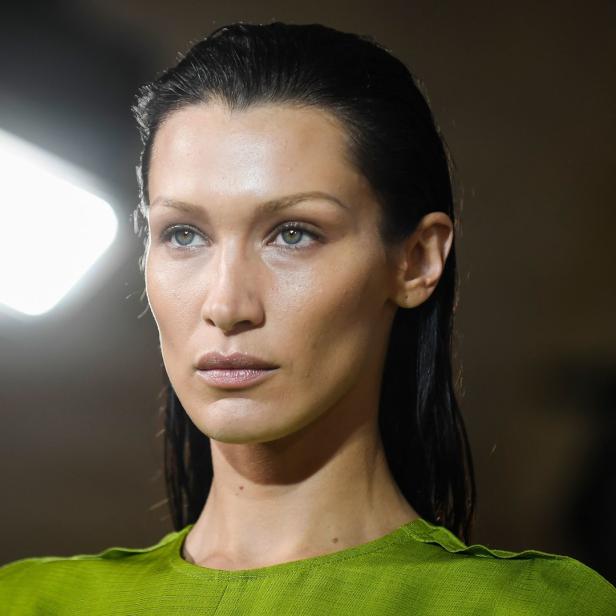 Bella Hadid mit zurückgekämmtem Haar und grünem Oberteil blickt zur Seite.