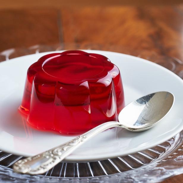Ein rotes Wackelpudding auf einem Teller mit einem Löffel daneben.