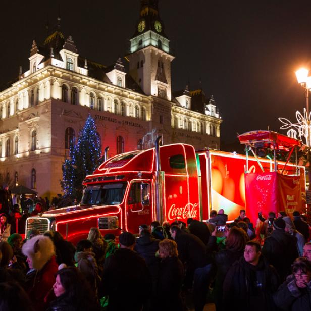 Ein beleuchteter Coca-Cola-Truck steht vor dem Rathaus auf einem belebten Platz.