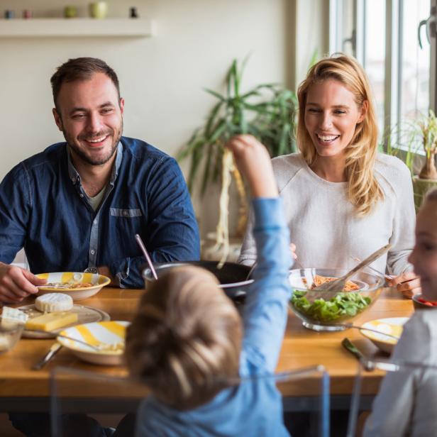 Eine Familie sitzt lächelnd beim Mittagessen am Tisch.