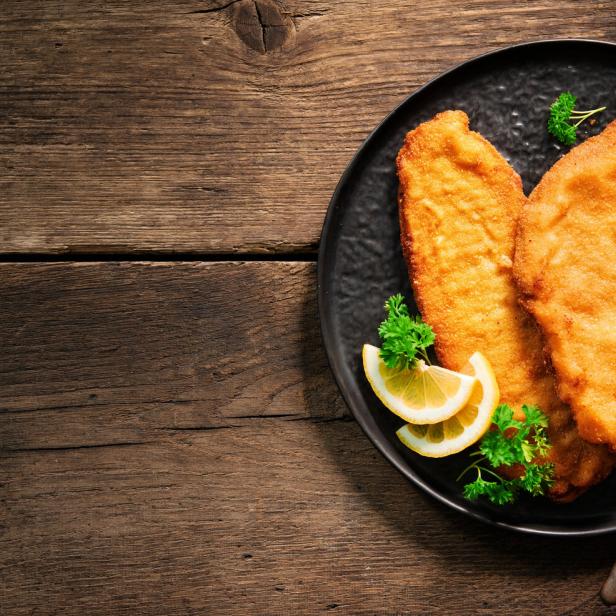 Zwei goldbraune Schnitzel auf einem Teller mit Zitrone und Petersilie angerichtet.