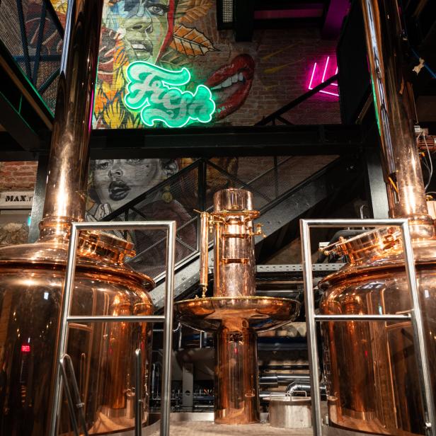Zwei große, glänzende Kupferkessel in einer Brauerei, im Hintergrund Wandmalereien und Neonlichter.