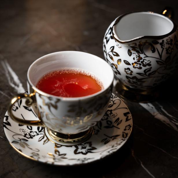 Eine Tasse Tee und ein Milchkännchen mit floralem Muster stehen auf einem Tisch.