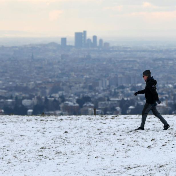 Eine Person geht auf einer schneebedeckten Wiese mit Blick auf die Stadt Wien.