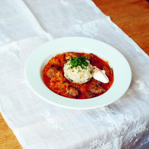 Ein Teller mit ungarischem Letscho, serviert mit einem Knödel und einem Klecks Schmand.