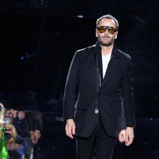 Tom Ford auf dem Laufsteg, gekleidet in einen schwarzen Anzug und Sonnenbrille.