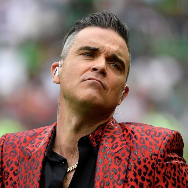 Robbie Williams trägt ein rot-schwarz gemustertes Jackett.