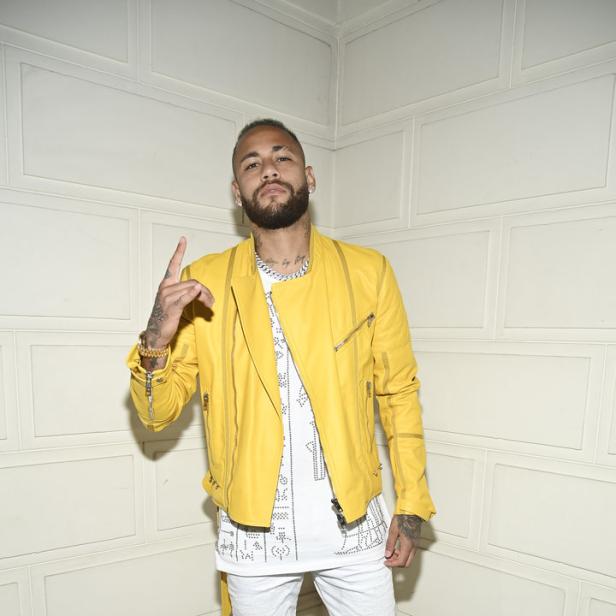 Neymar posiert in gelber Jacke, weißem Oberteil und weißen Hosen für ein Foto.