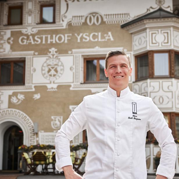 Ein lächelnder Koch steht vor dem Gasthof Yscla.