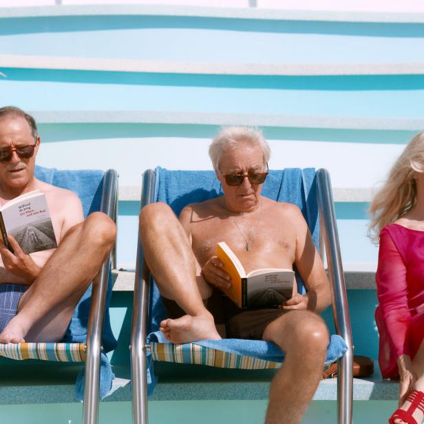 Drei ältere Personen entspannen am Pool und lesen das Buch „Wilfried de Jong – Ein Mann und sein Rad“.