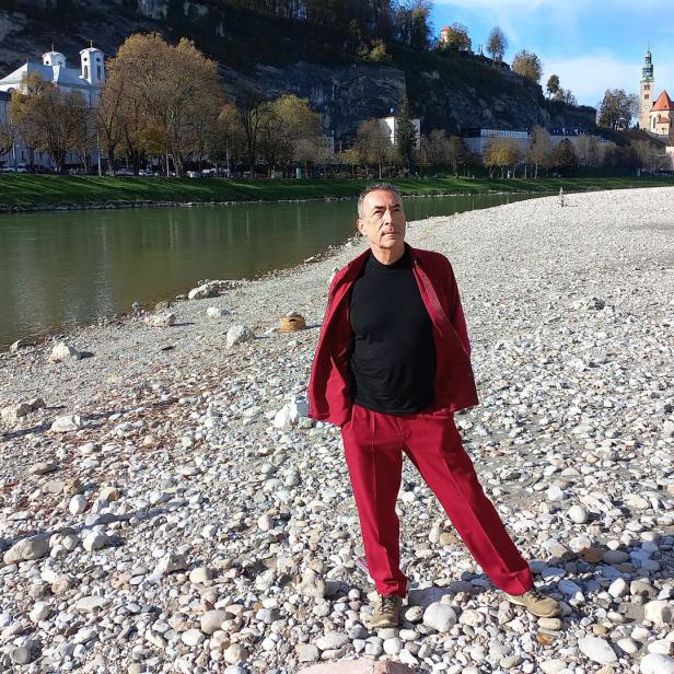 Ein Mann in rotem Anzug steht am Ufer der Salzach in Salzburg.
