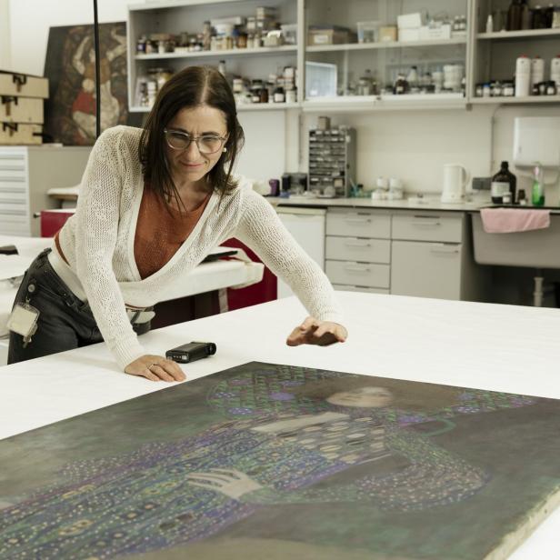 Eine Restauratorin untersucht ein Gemälde von Gustav Klimt auf einem Tisch.