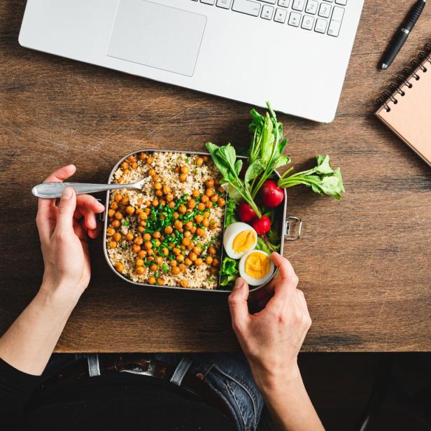 Eine Person isst eine Mahlzeit mit Kichererbsen, Quinoa, Radieschen und Ei am Schreibtisch.