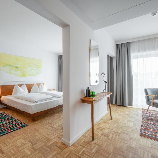 Ein helles Hotelzimmer mit Doppelbett, Sessel und Holzboden.