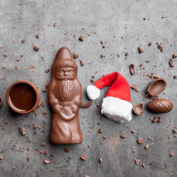 Ein Schokoladennikolaus, Schokoladeneier und ein Weihnachtsmannhut liegen auf einer grauen Oberfläche.