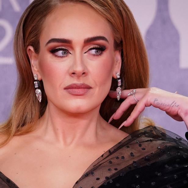 Die Sängerin Adele mit Ohrringen und einem Tattoo auf der Hand.