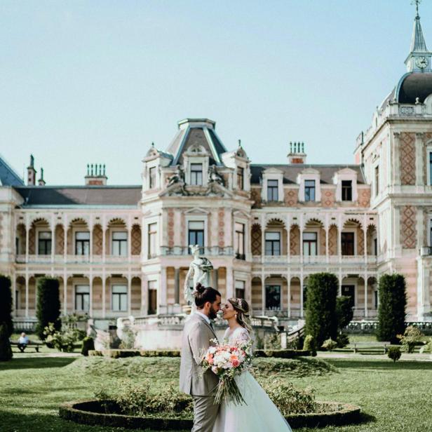 Ein Brautpaar steht vor einem Schlossgarten mit großem Schloss.