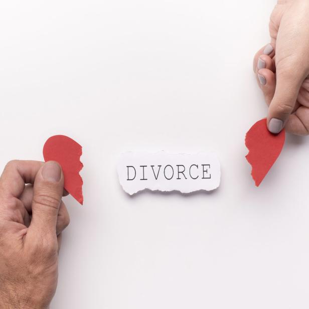 Zwei Hände halten Teile eines zerrissenen roten Herzens neben dem Wort „Divorce“.
