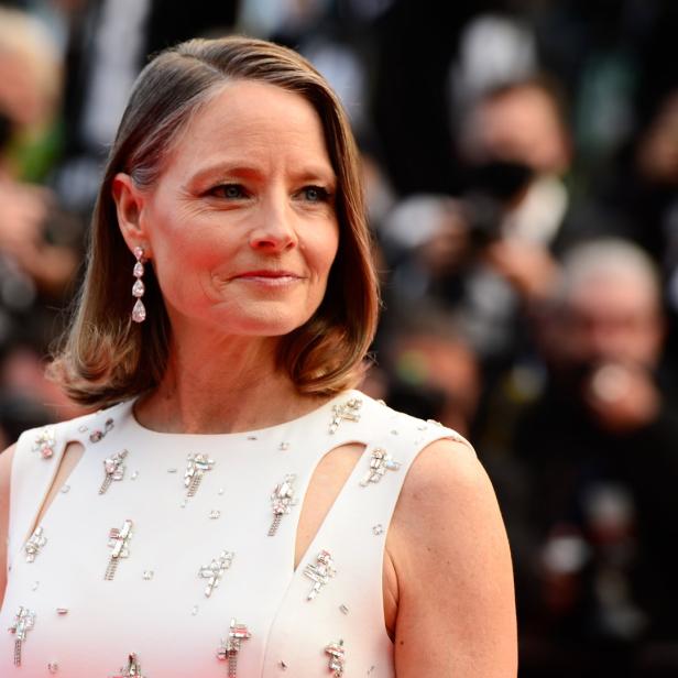 Jodie Foster auf einem roten Teppich in einem weißen Kleid mit Schmucksteinen.