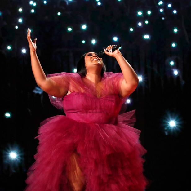 Lizzo singt in einem pinkfarbenen Tüllkleid auf einer Bühne mit Lichtern.