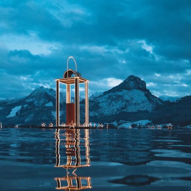 Eine beleuchtete Laterne steht auf dem Wasser vor einer Bergkulisse.