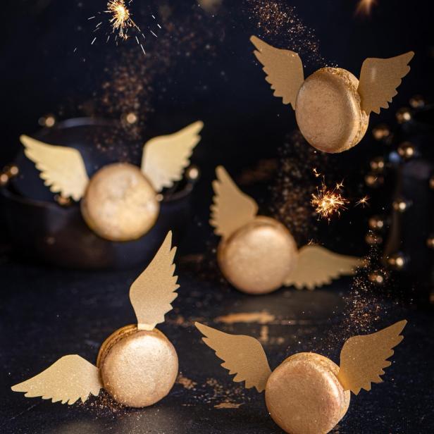 Goldene Macarons mit Flügeln und Wunderkerzen auf dunklem Hintergrund.