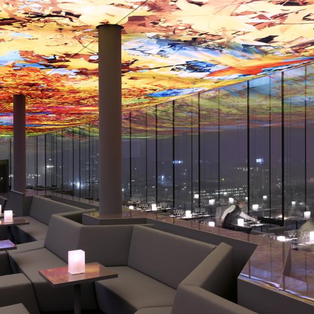 Ein Restaurant mit farbenfroher Deckenkunst und Blick auf eine Stadt bei Nacht.