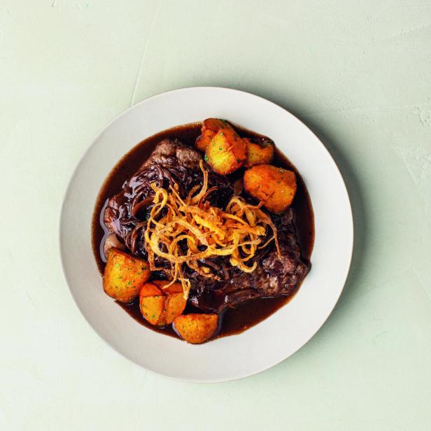 Ein Teller mit Schmorbraten, Kartoffeln und Röstzwiebeln in dunkler Soße.