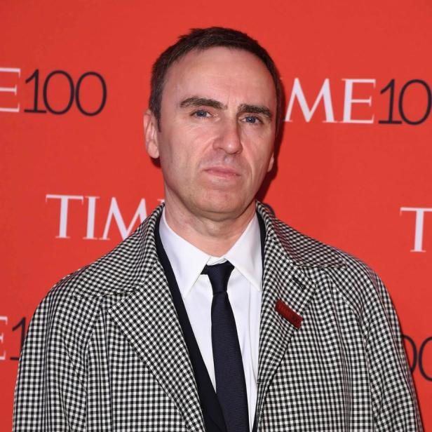 Raf Simons trägt einen karierten Mantel vor einem roten „Time 100“-Hintergrund.
