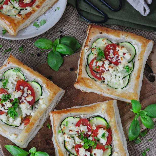 Blätterteig-Tartelettes belegt mit Zucchini, Tomaten und Feta auf einem Holztisch.