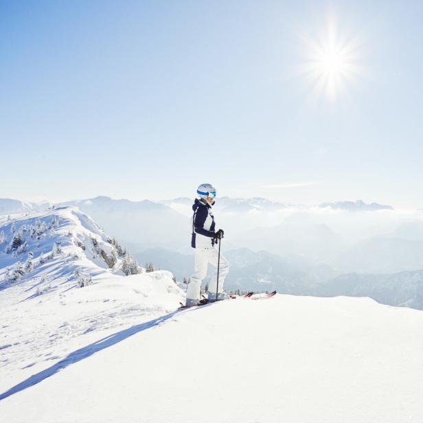 Eine Skifahrerin genießt die Aussicht auf die verschneiten Berge an einem sonnigen Tag.