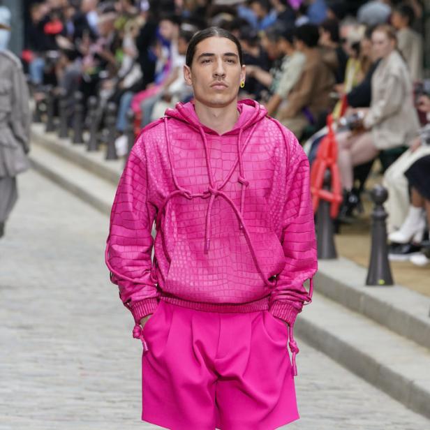 Ein Mann in einem pinkfarbenen Hoodie und Shorts läuft auf einem Laufsteg.