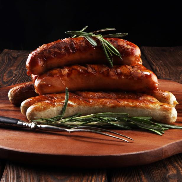 Mehrere gegrillte Würstchen sind auf einem Holzbrett mit Rosmarin angerichtet.