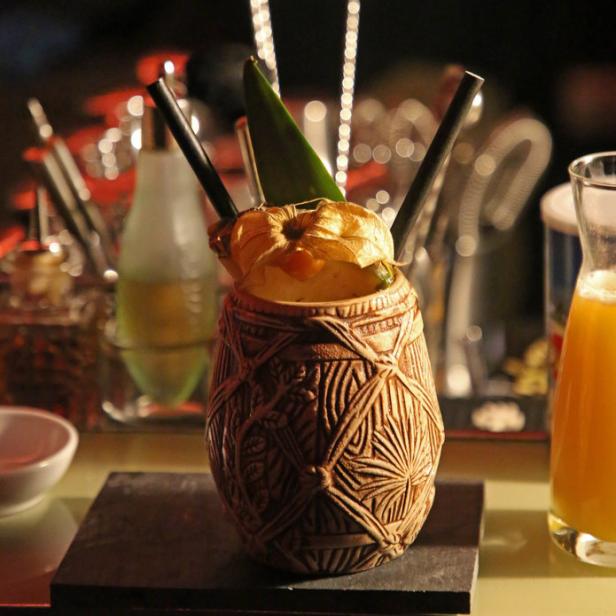 Ein exotischer Cocktail in einem Tiki-Becher, garniert mit einer Physalis und einem Blatt.