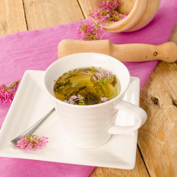 Eine Tasse Kräutertee mit rosa Blüten auf einem Holztisch.