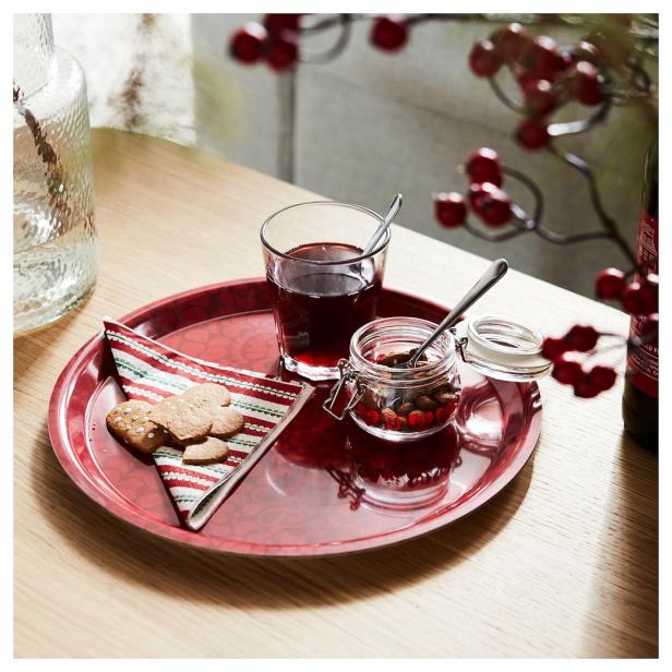 Ein rotes Tablett mit Keksen, einem Glas Saft und einem Glas mit Nüssen und Beeren.