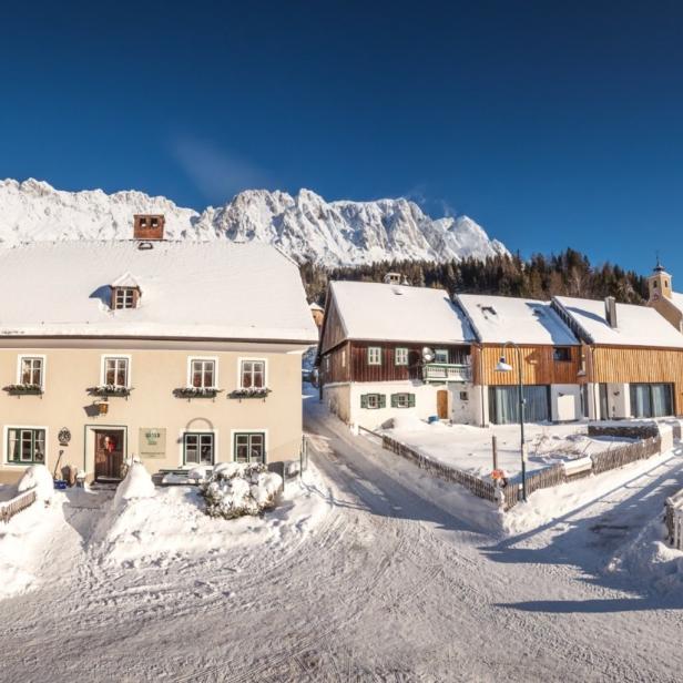 Winterliche Landschaft mit schneebedeckten Häusern und Bergen im Hintergrund.