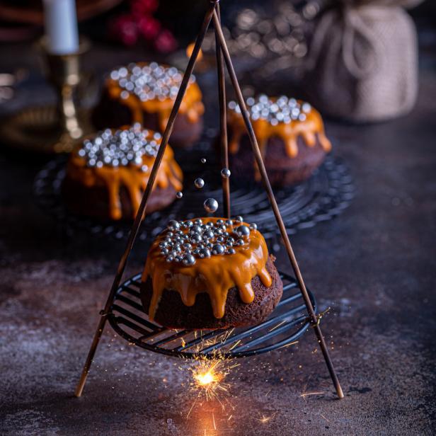 Ein festlicher Schokoladenkuchen mit Karamellglasur und silbernen Zuckerstreuseln wird mit einer Wunderkerze präsentiert.