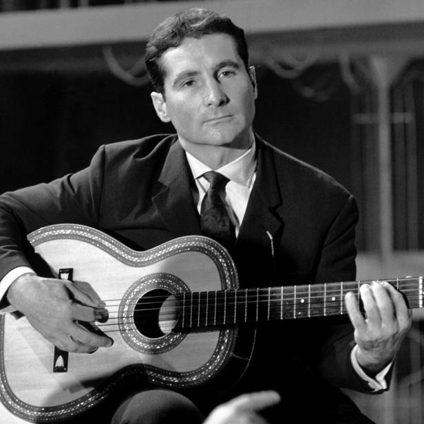 Ein Mann im Anzug spielt auf einer verzierten Gitarre.