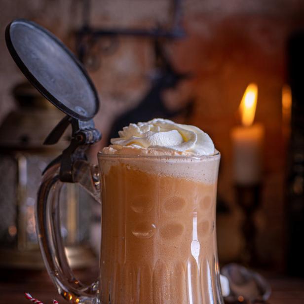 Ein Glas Kürbis-Latte mit Schlagsahne und Zimtstangen auf einem Holztisch.