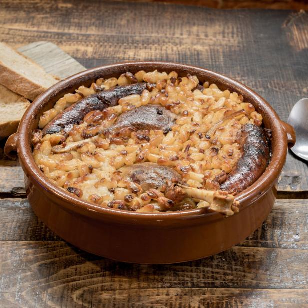 Ein Cassoulet mit Wurst und Entenkeule in einer braunen Keramikform.