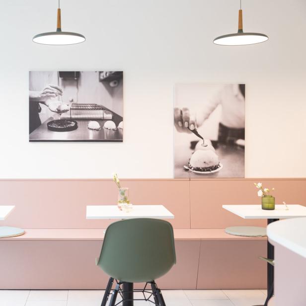 Innenansicht eines Cafés mit Tischen, Stühlen und Schwarz-Weiß-Fotografien an der Wand.