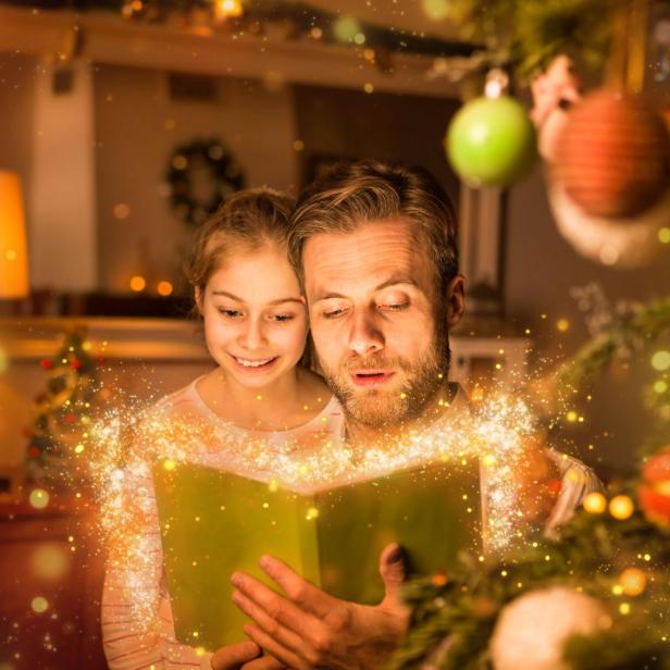 Ein Vater liest seiner Tochter zu Weihnachten zu Hause aus einem Buch vor.