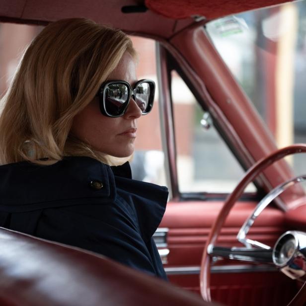 Eine Frau mit Sonnenbrille sitzt in einem roten Oldtimer.