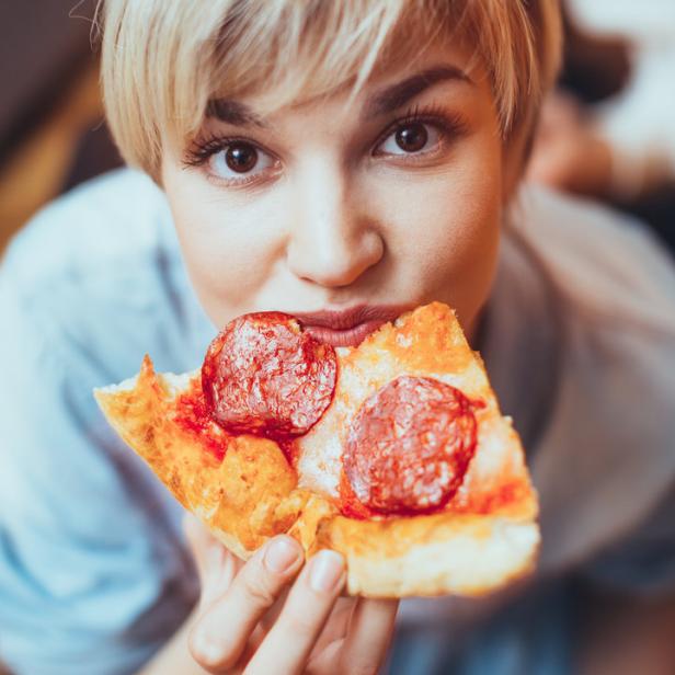 Eine Frau mit Rentier-Haarreif isst ein Stück Pizza mit Salami.