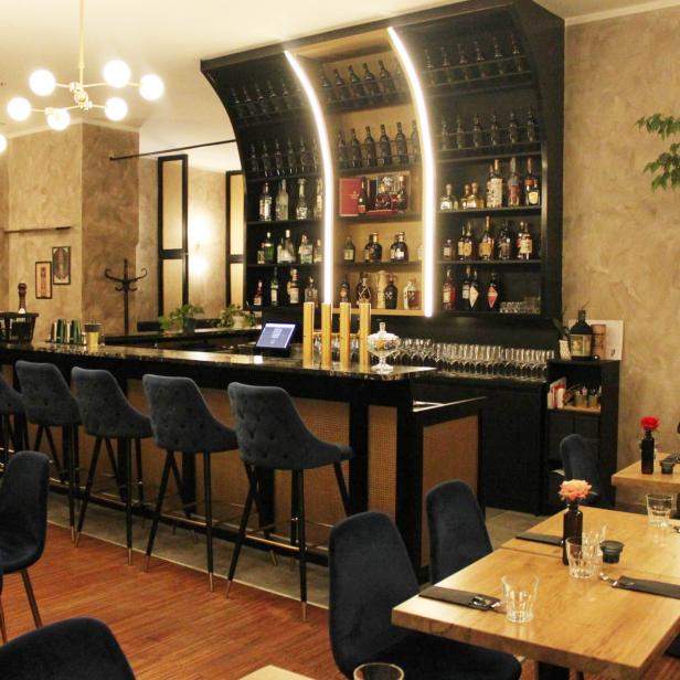 Innenansicht einer Bar mit dunklen Möbeln und blauem Samtbezug.
