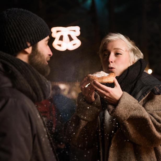 Eine Frau isst einen Kopfingkrapfen auf einem Weihnachtsmarkt.