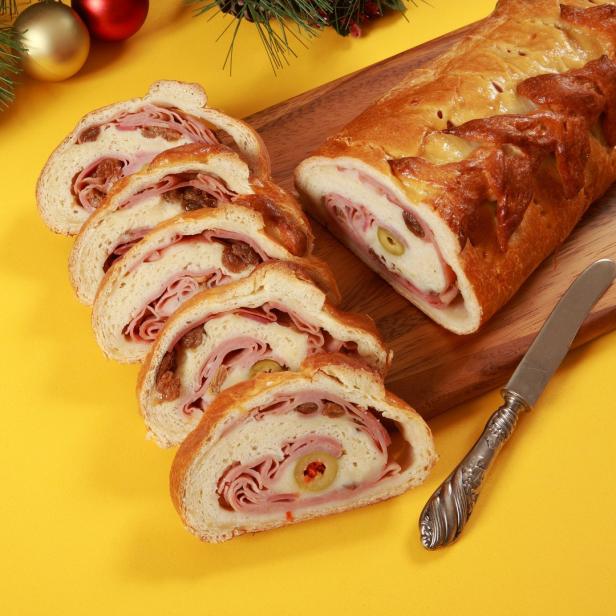 Ein aufgeschnittener Weihnachtsstollen mit Schinken, Oliven und Rosinen auf einem Holzbrett.