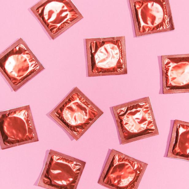 Mehrere Kondompackungen liegen auf einem rosa Hintergrund.